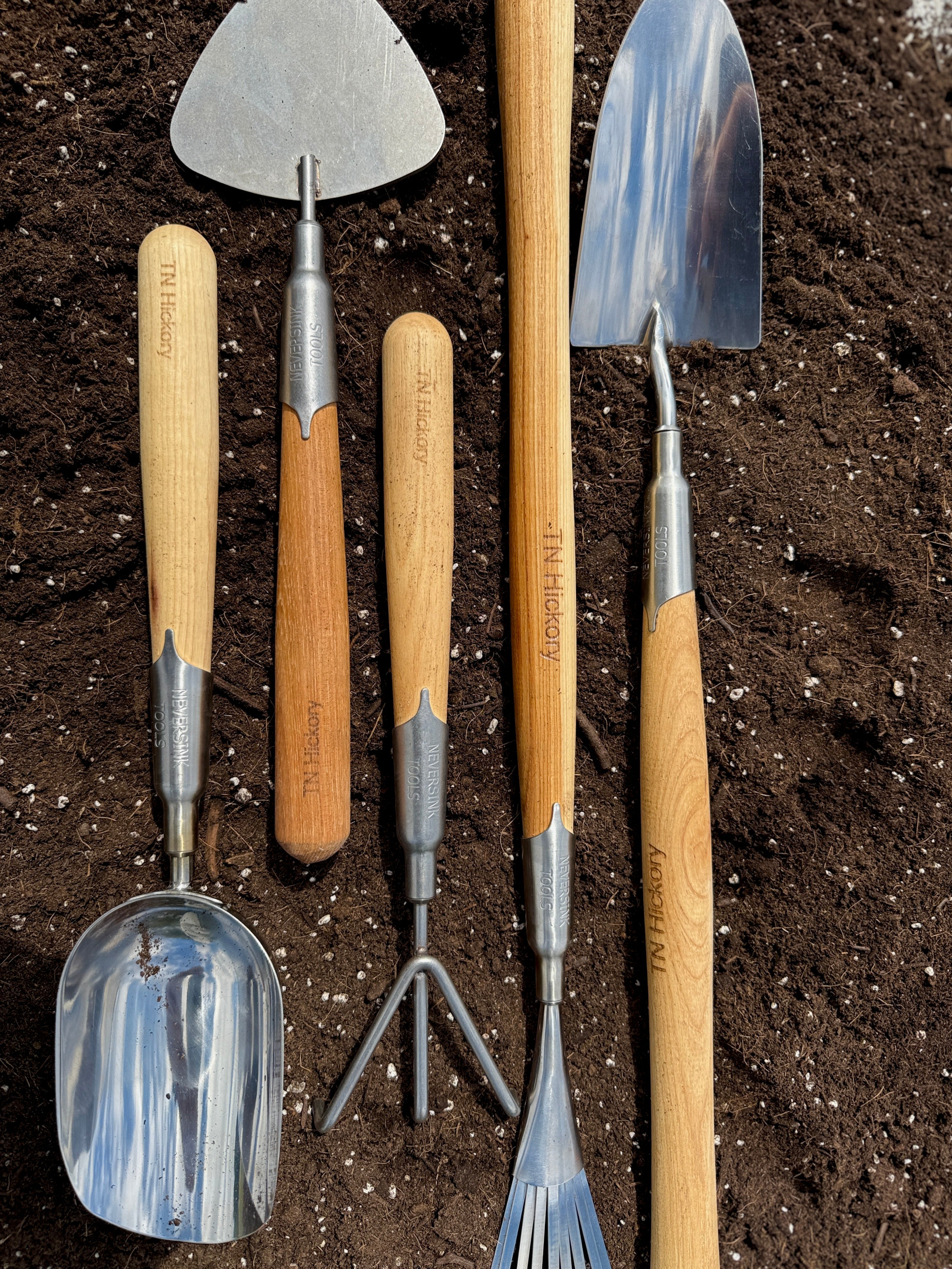Set of gardening tools with wooden handles on a soil background