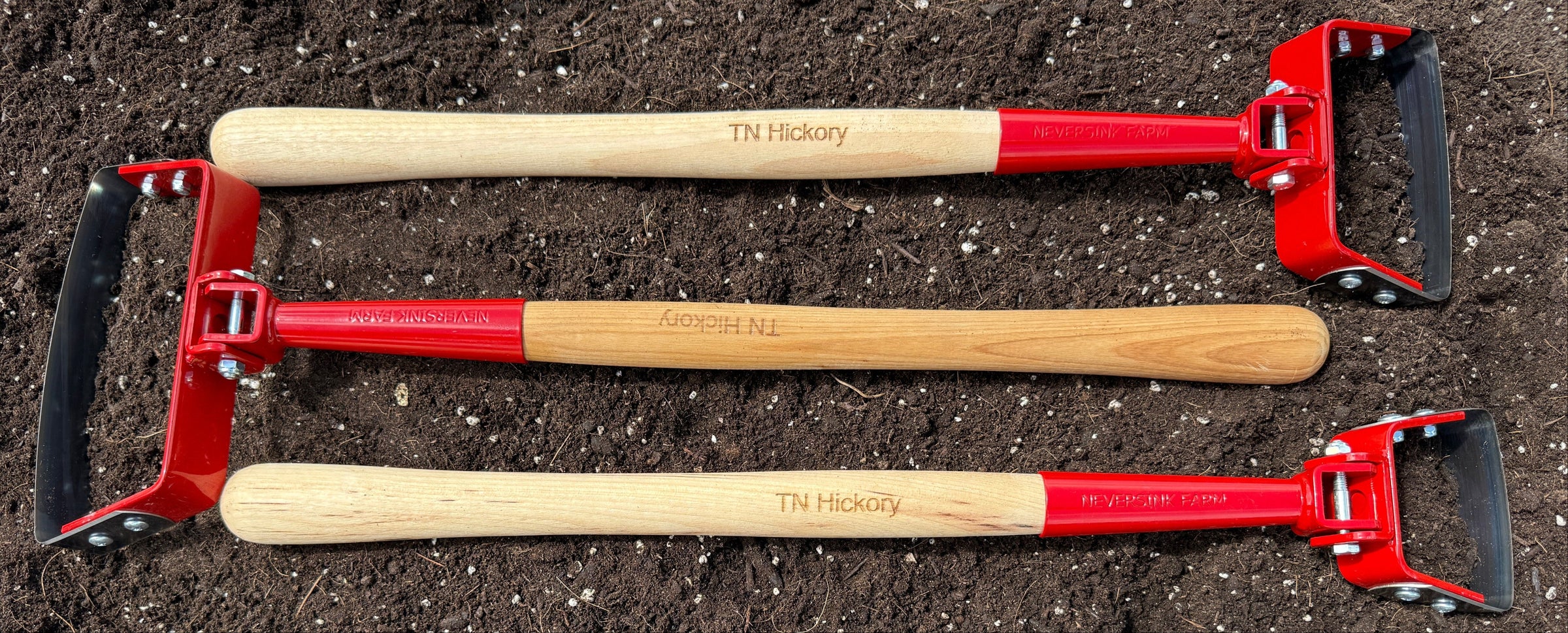 Three garden tools with red handles and black ends on a bed of soil.