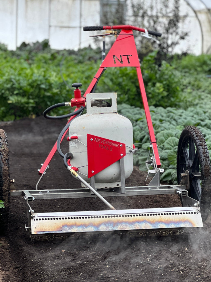 A red and silver flame weeder with a white tank, attached to a frame with wheels, designed for weed control in fields.